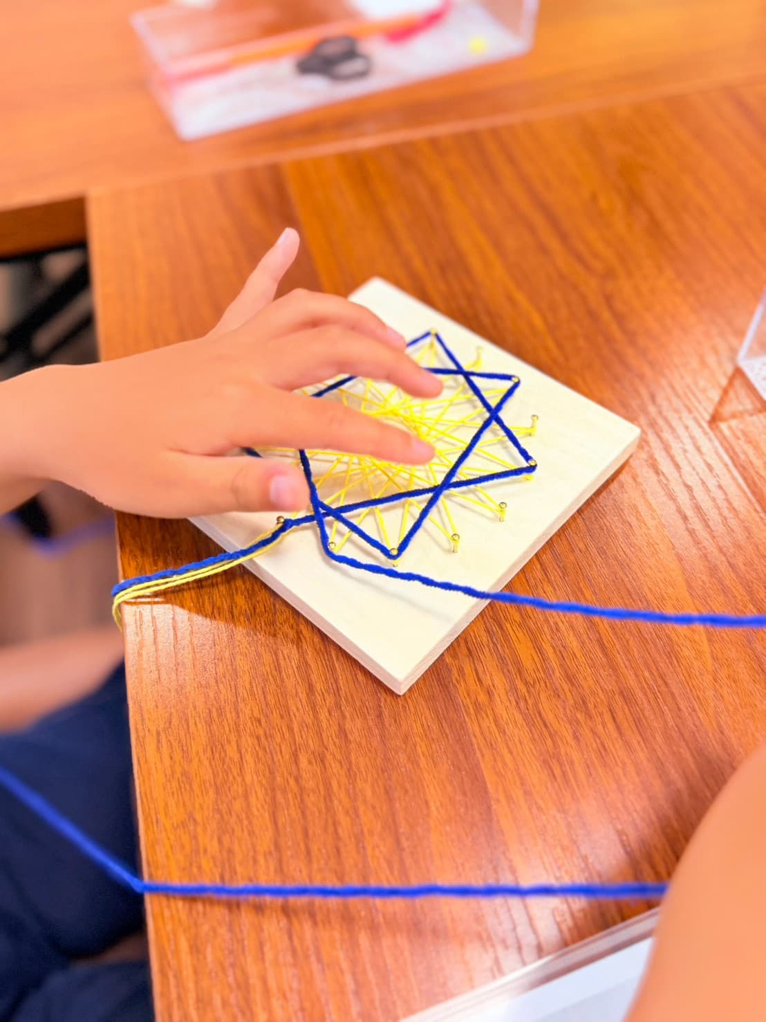 糸かけ曼荼羅の板に糸をかけて模様を作る子どもの手元
