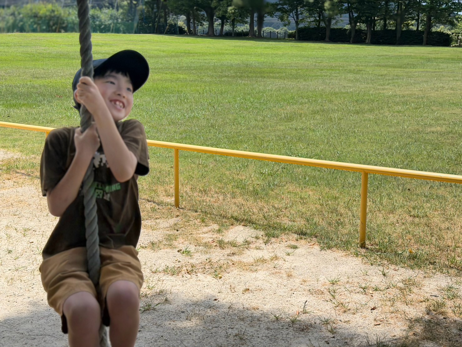 公園の遊具でロープにつかまり笑顔を見せる小学生